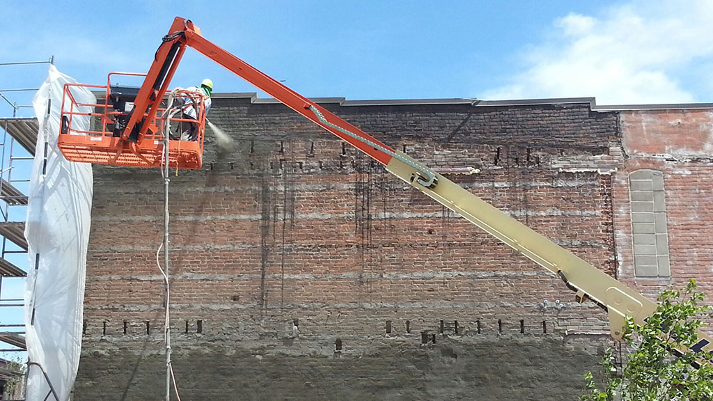 Western Specialty Contractors worker sprays shotcrete on the entire west elevation of the historic Norden Hall building repurposed as a wine bar in Des Moines, Iowa. Once the new concrete had cured, a textured acrylic coating was applied to waterproof the wall and maintain its historic appearance.